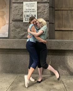 two young women hugging each other in front of a wall with a sign on it