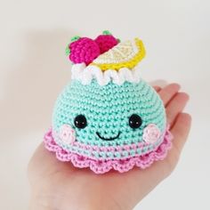 a hand holding a small crocheted toy with a cupcake on it's head