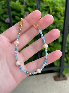 a hand holding a blue and white beaded bracelet with gold accents on it's fingers