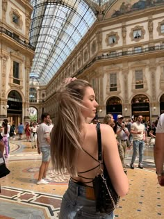 a woman with long hair standing in an indoor shopping mall looking up at the ceiling