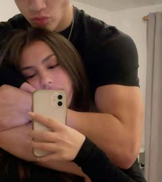 a man and woman hugging each other while looking at a cell phone screen with their eyes closed