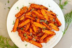 a white plate topped with cooked carrots covered in marinara sauce and garnished with parsley