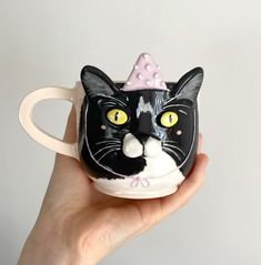 a hand holding a black and white cat mug with a pink bow on it's head