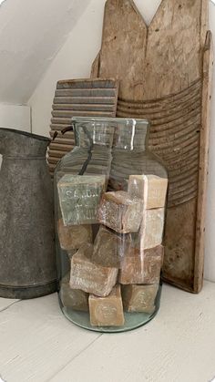 a glass jar filled with blocks of wood sitting on top of a white table next to a metal bucket