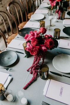 the table is set with plates, silverware and pink flowers in vases on it