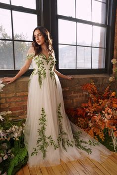 a woman standing in front of a window wearing a white dress with green leaves on it