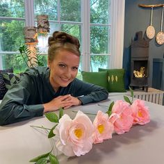 a woman sitting at a table with flowers in front of her and smiling for the camera