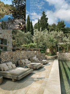 an outdoor lounge area next to a pool with water running through it and trees in the background