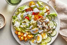 a white plate topped with salad and dressing next to a glass of green juice on top of a table