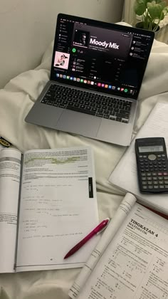 a laptop computer sitting on top of an open book next to a calculator