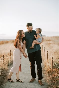 a family walking down a path holding their toddler's hand and looking at the camera