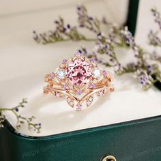 a pink diamond ring sitting on top of a green box next to purple and white flowers