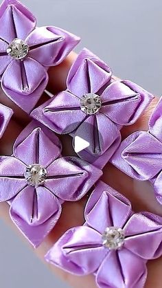 a hand is holding several purple flowers with diamonds on the center, and two are being held by someone's fingers