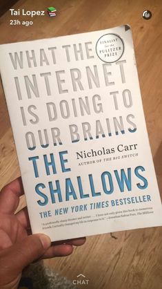 a person holding up a book in front of a wooden table with the title what the internet is doing to our brain