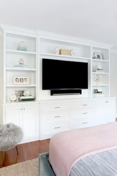 a large flat screen tv mounted to the side of a white bookcase in a bedroom