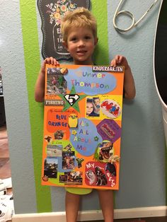 a young boy holding up a poster with pictures on it in front of a green and blue wall