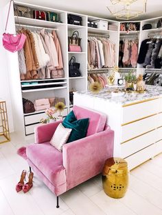 a pink couch sitting in front of a white closet filled with clothes and handbags