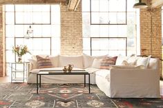 a living room filled with lots of furniture next to large windows on the side of a brick wall