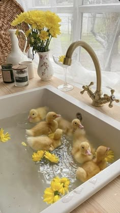 four little ducks in a sink with yellow flowers on the counter and water running from it