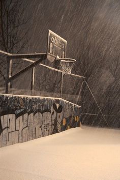 a basketball court covered in snow next to a building with graffiti on the walls and trees