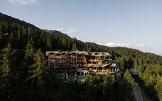 an aerial view of a large building in the middle of some trees and mountains,