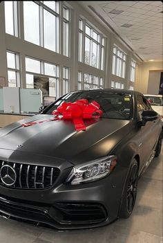 a car with a red bow on the hood in a showroom filled with cars