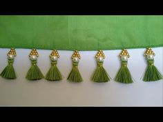 six tassels with pearls and gold beads on green velvet fabric, lined up in a row