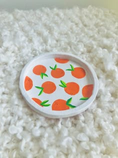 a plate with oranges painted on it sitting on top of a pile of white yarn