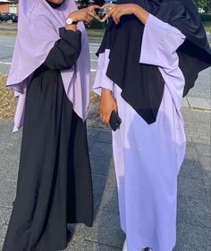 two women standing next to each other on a sidewalk with buildings in the background and one wearing a purple shawl