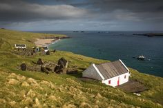 a small white house sitting on top of a lush green hillside next to the ocean