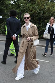 a woman in a trench coat and white pants is walking down the street with other people