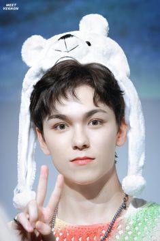 a young man with a white bunny hat on his head making the peace sign while standing in front of a blue background