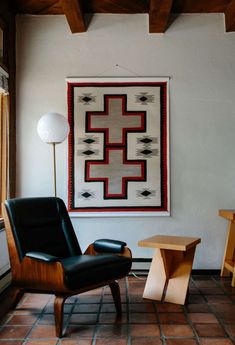 a chair and table in a room with a rug hanging on the wall above it