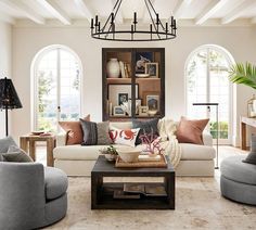 a living room filled with lots of furniture next to two large windows and a chandelier