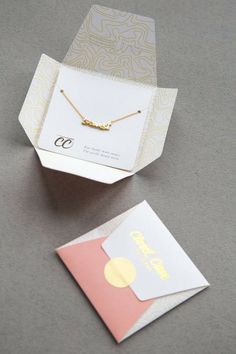 an open box with a necklace on it and a card in the bottom right corner