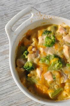 a white bowl filled with broccoli, chicken and cheese soup on top of a wooden table