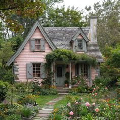 a pink house with green shutters and flowers around it