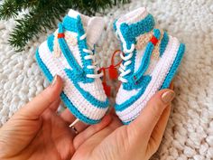 someone is holding up a crocheted pair of blue and white sneakers with orange laces