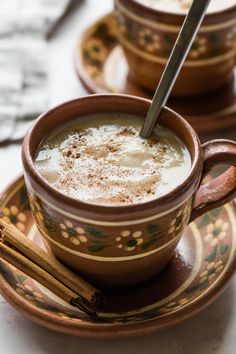 two cups of hot chocolate with cinnamon sticks on the saucer and another cup in the background