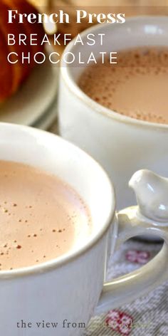 two white cups filled with hot chocolate on top of a table