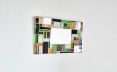 a mirror mounted to the side of a wall with different colored tiles on it's sides