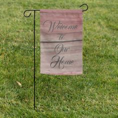 a welcome to our home sign in the grass with a flag hanging from it's pole