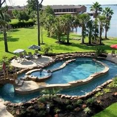 an outdoor swimming pool surrounded by lush green grass and palm trees next to the water