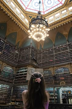 a woman standing in front of a library filled with books and chandelier hanging from the ceiling