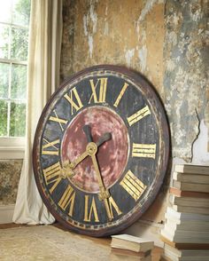 an old clock sitting on top of a table next to a stack of books in front of a window