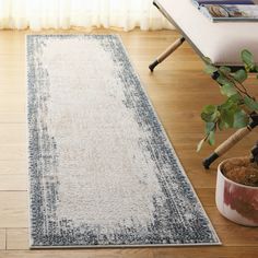 a white and blue area rug on a wooden floor next to a potted plant