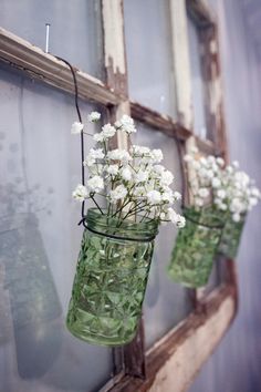 three mason jars filled with white flowers hanging from a window