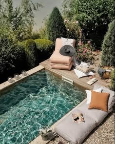 an outdoor swimming pool with chaise lounges and pillows on the ground next to it