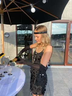 a woman is standing under an umbrella and pouring wine into a glass at a table