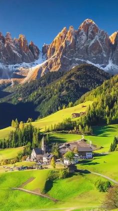 the mountains are covered in snow and green grass, while houses stand on either side